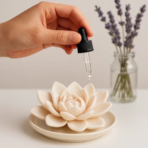 Hand applying essential oil with dropper onto a white plaster lotus flower diffuser, with lavender in the background – perfect for natural aromatherapy at home