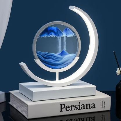 Blue sand art LED lamp with circular frame and cascading sand design, placed on books in a modern home interior – ideal for decorative lighting and relaxation